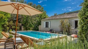 A swimming pool with lounge chairs and an umbrella, surrounded by greenery and a house. - Casa Murati (Sisco)