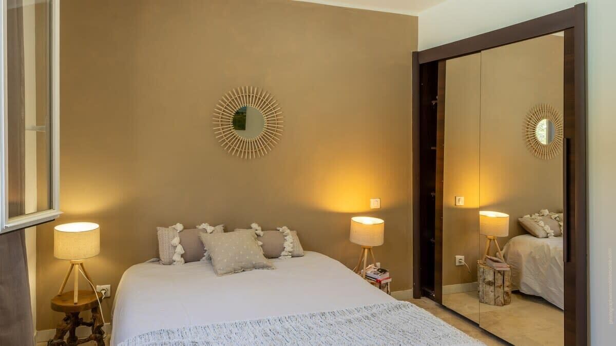 Une chambre à coucher avec un grand lit, deux lampes de chevet, un miroir et un luminaire décoratif fixé au mur.