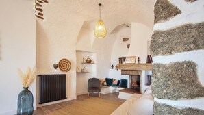 Ein gemütliches Wohnzimmer mit Steinwand, Kamin, einer bequemen Couch und einer Pendelleuchte.
