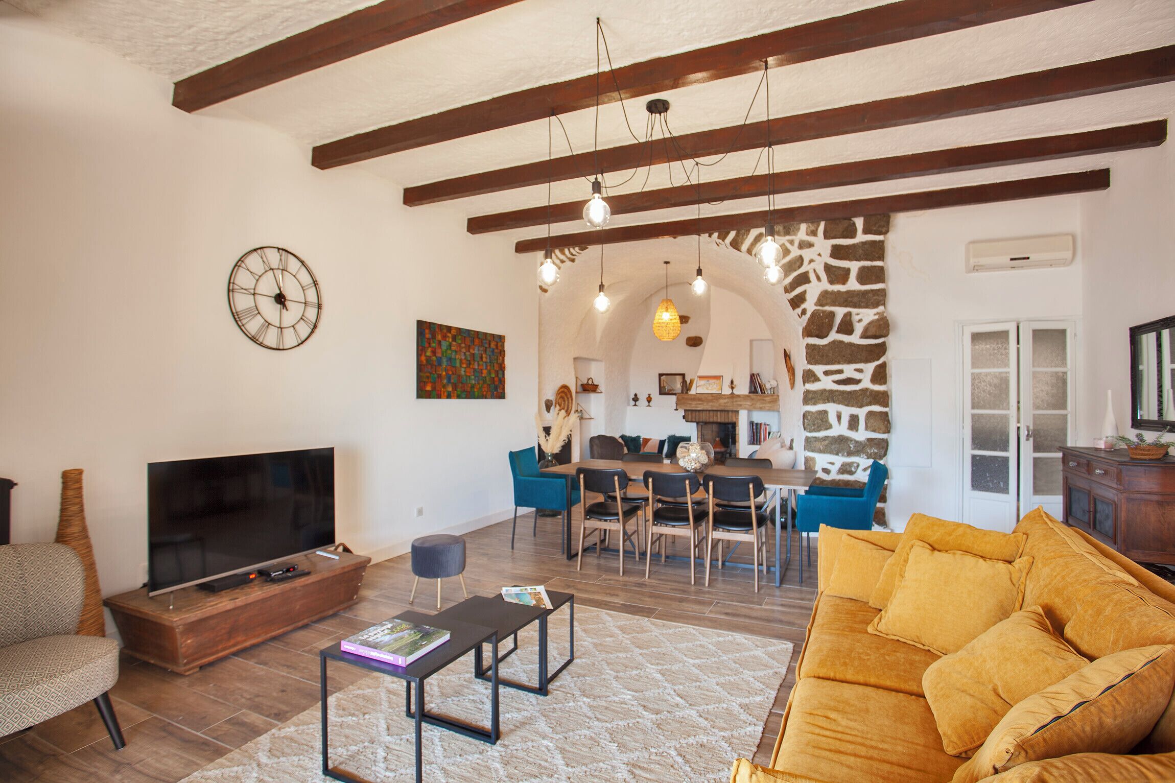 A living room with a TV, sofa, coffee table, and dining area with chairs.