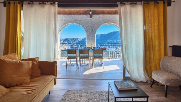 Ein Wohnzimmer mit einer Couch, einem Couchtisch und Blick auf einen Balkon mit Sitzgelegenheit und einem malerischen Bergpanorama.