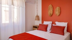 A bedroom with a bed, white curtains, a hanging lamp, and two wall decorations. - Casa Félicie (Calvi)