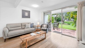 A modern living room with a sofa, coffee table, and a view of a garden through a sliding glass door.