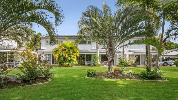 A well-maintained lawn, palm trees, and a two-story building with a covered patio area.