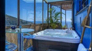 A hot tub in a room with large windows, a glass table, and a view of the hills. - Casa Di A Scala (Brando)