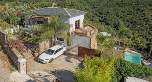 A modern house with a white car parked in front, surrounded by lush greenery and a swimming pool.