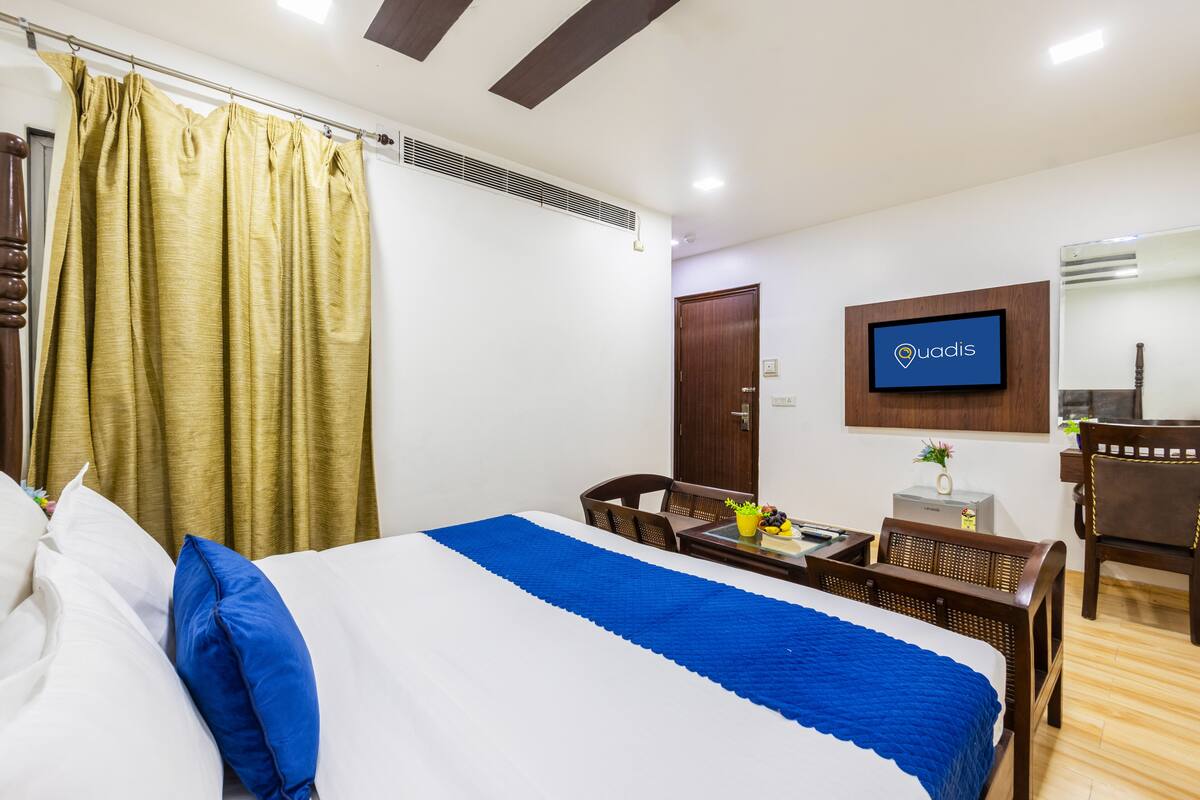 Une chambre d’hôtel comprenant un lit, un bureau, une chaise, un téléviseur et une armoire en bois.