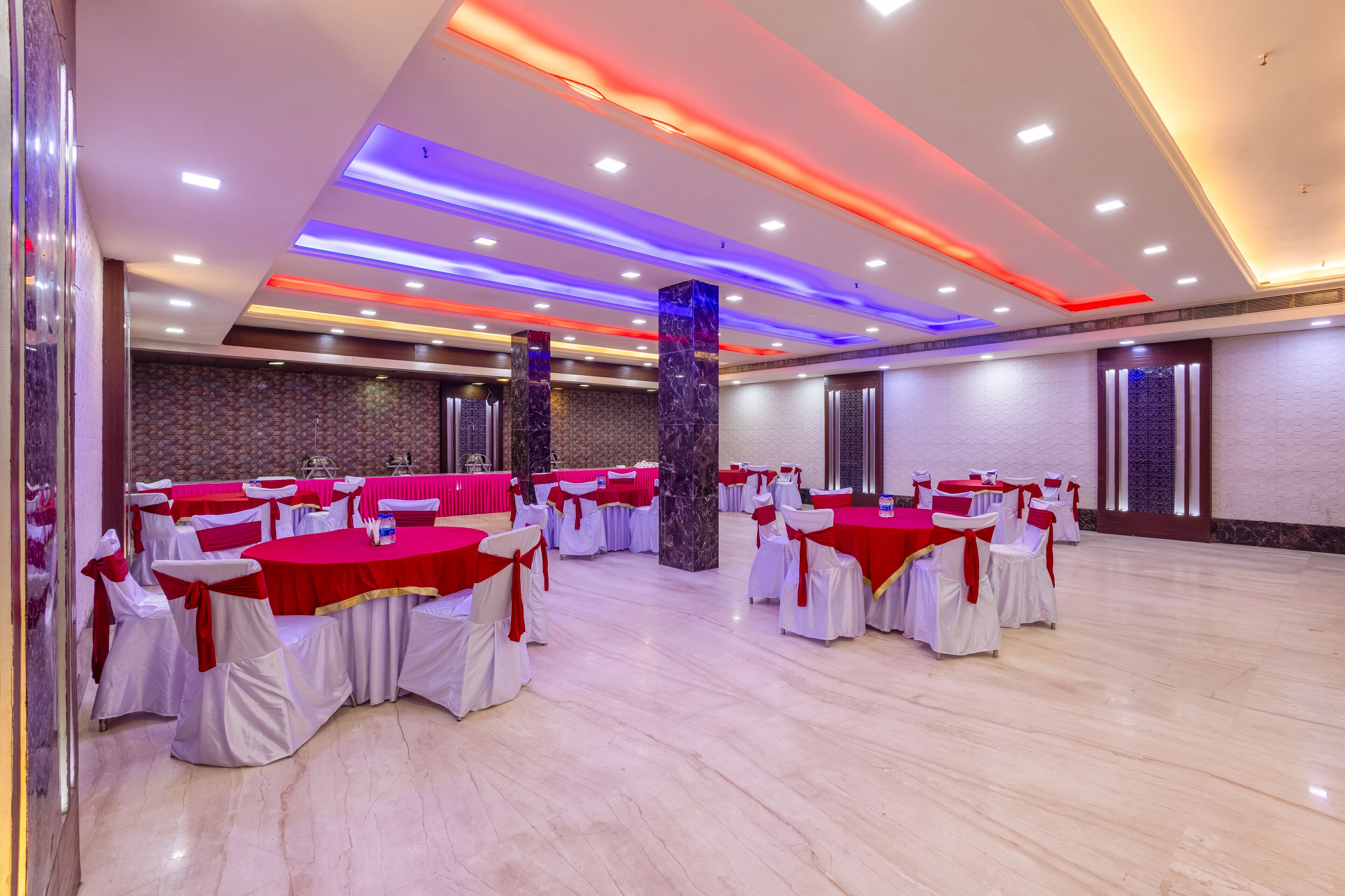 A spacious hall with multiple round tables, each covered with a red tablecloth and white chairs, and a marble floor.