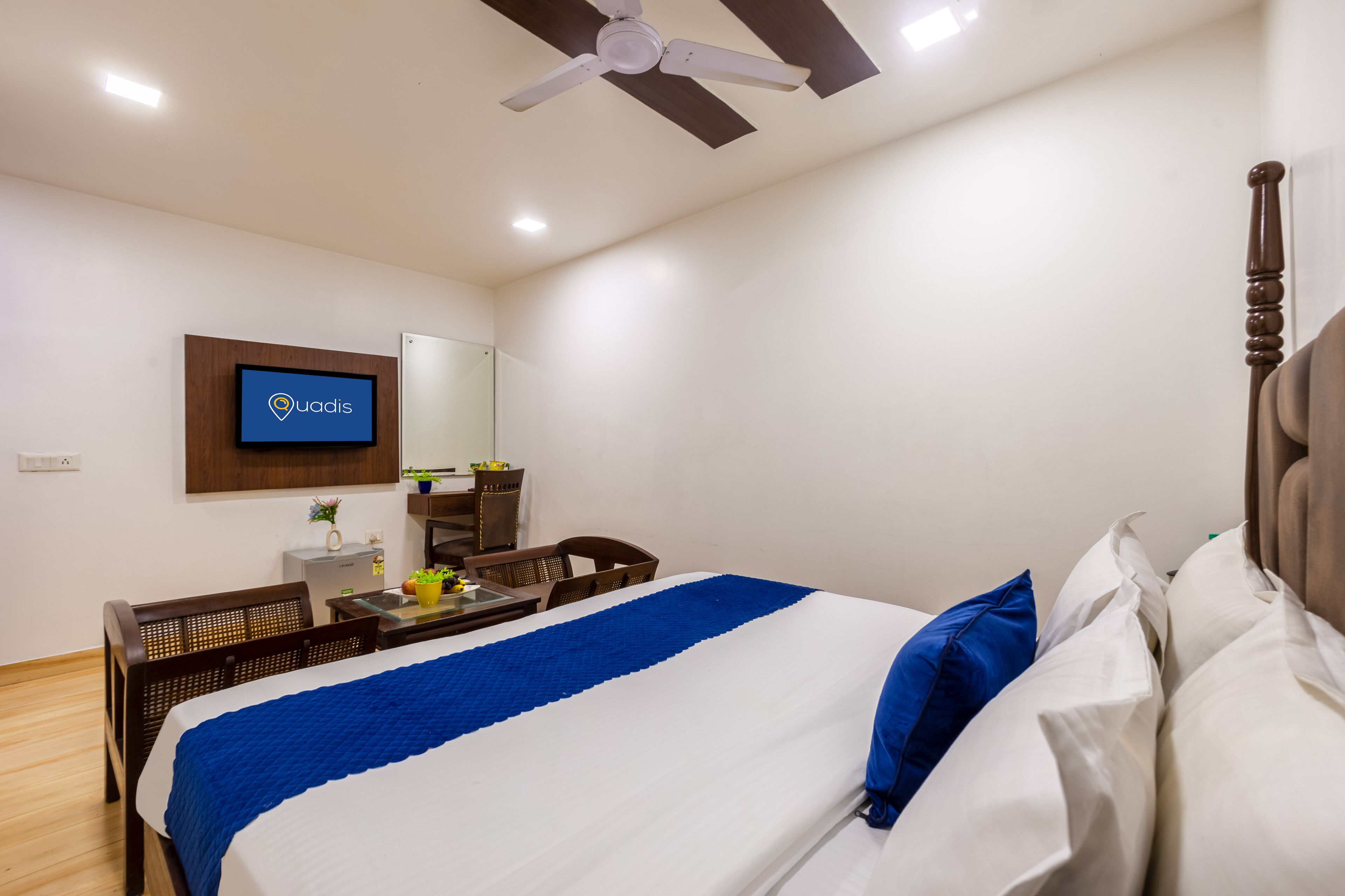 A hotel room with a bed, a desk, a chair, a television, and a ceiling fan.