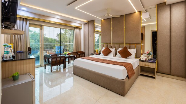A modern hotel room with a large bed, a desk, a chair, a dining table, and a balcony with a view.