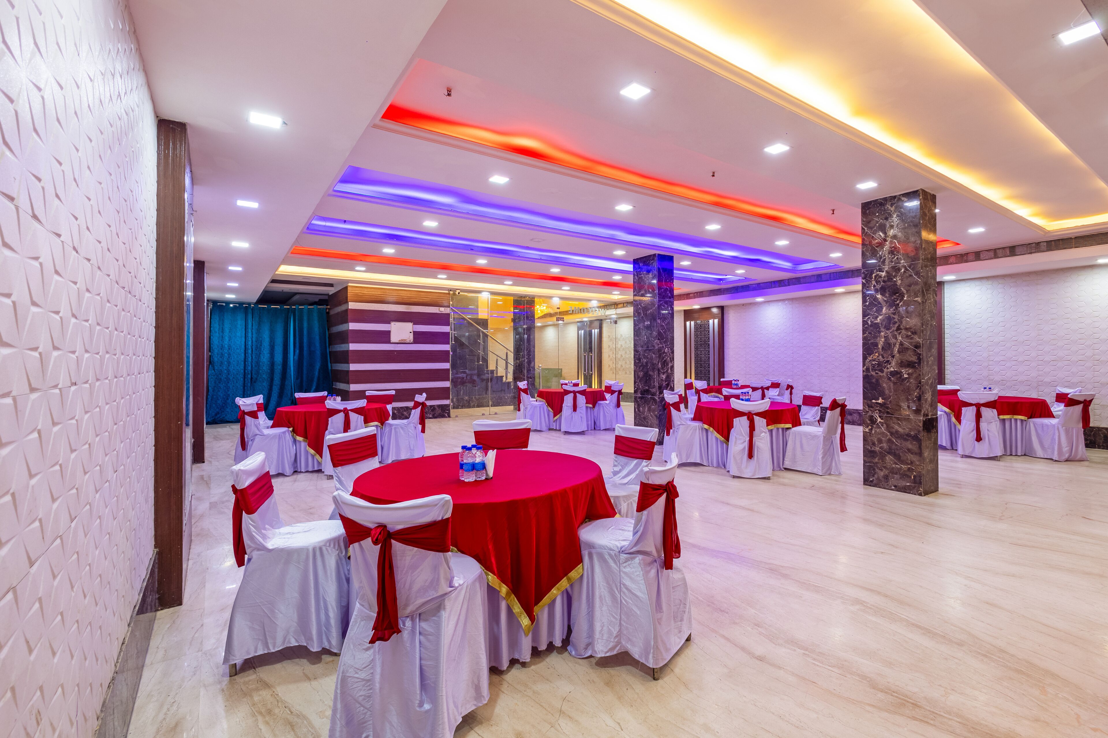 A banquet hall with round tables, white chairs with red sashes, and a marble pillar.