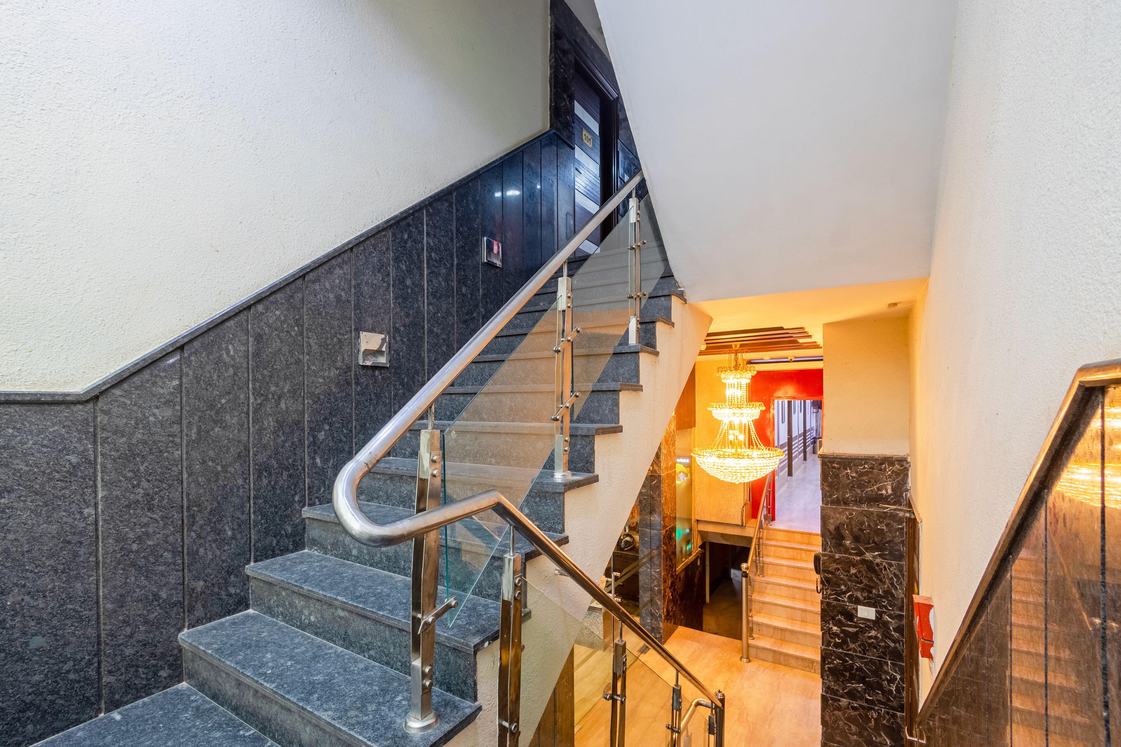Een moderne trap met glazen leuning en een handrail, die leidt naar een goed verlichte ruimte met een kroonluchter.