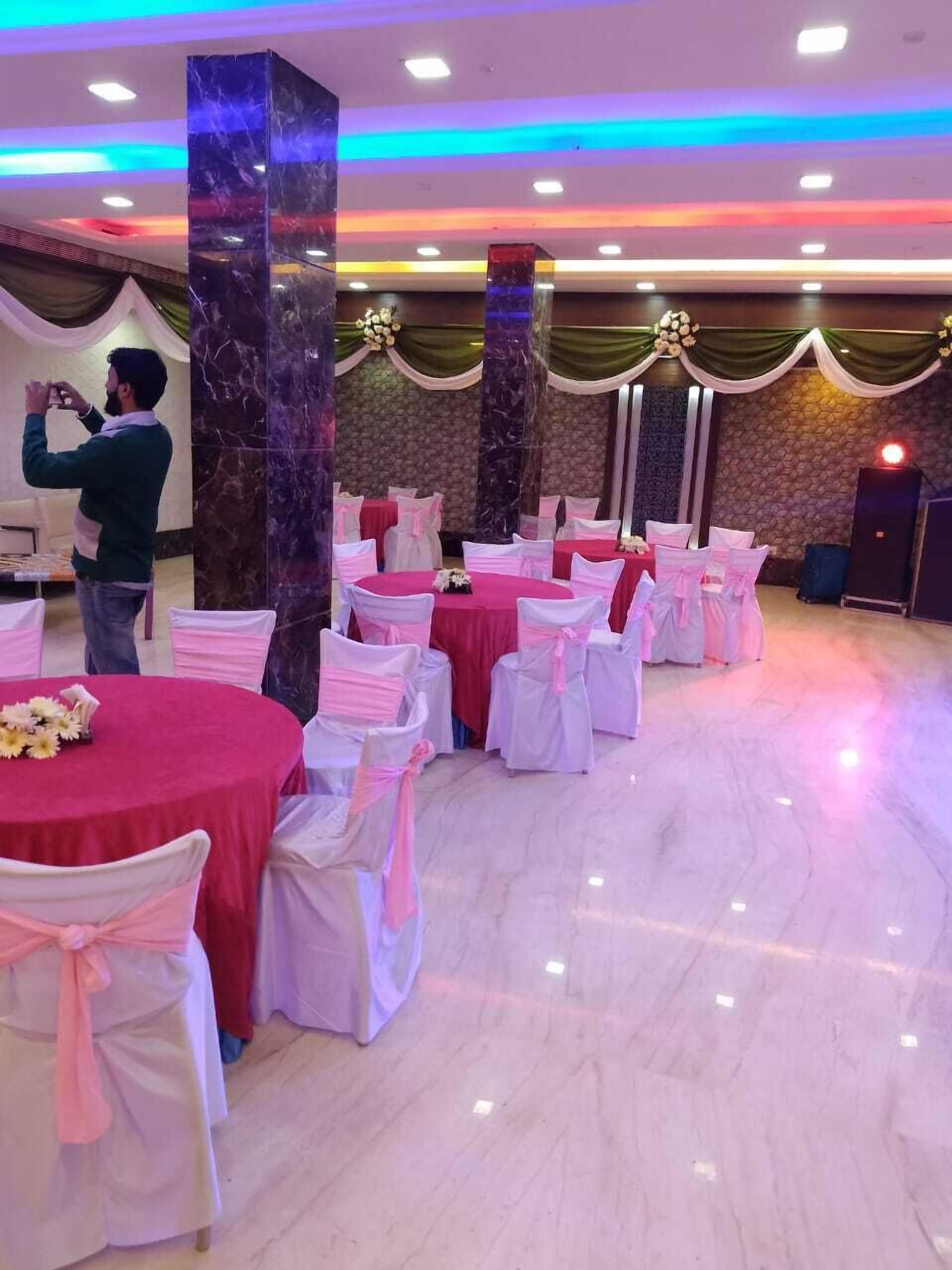 A banquet hall with round tables covered in red tablecloths and white chairs with pink sashes.