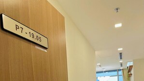 Un corridoio d'hotel con una porta in legno con l'indicazione P7-19.05, che conduce a una stanza con vista sulla città.