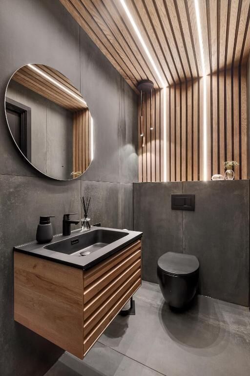 A modern bathroom with a wooden vanity, a round mirror, and a black toilet.