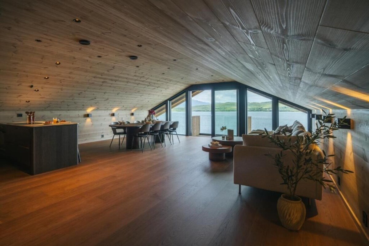 Ein geräumiges Zimmer mit Holzboden, einem Essbereich, einer Couch und einem großen Fenster mit Blick auf das Wasser.