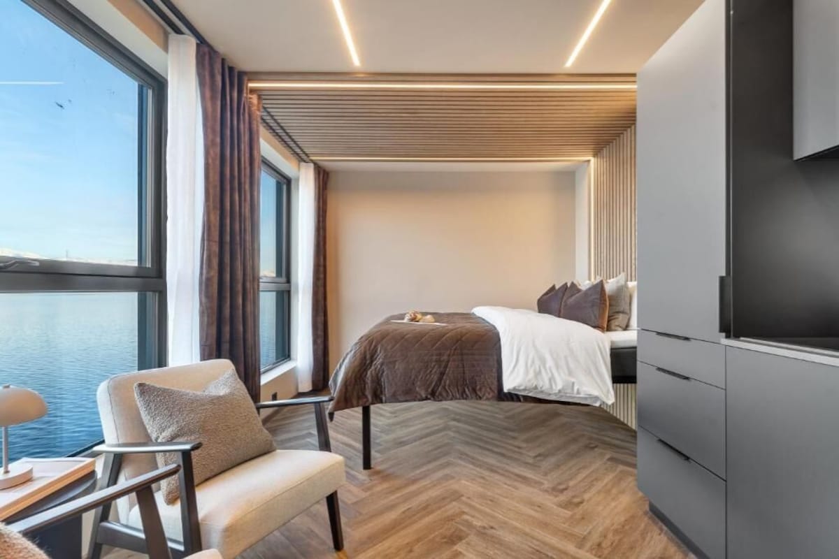 Ein modernes Hotelzimmer mit großem Fenster, einem Bett, einem Sessel und einem Fernseher.