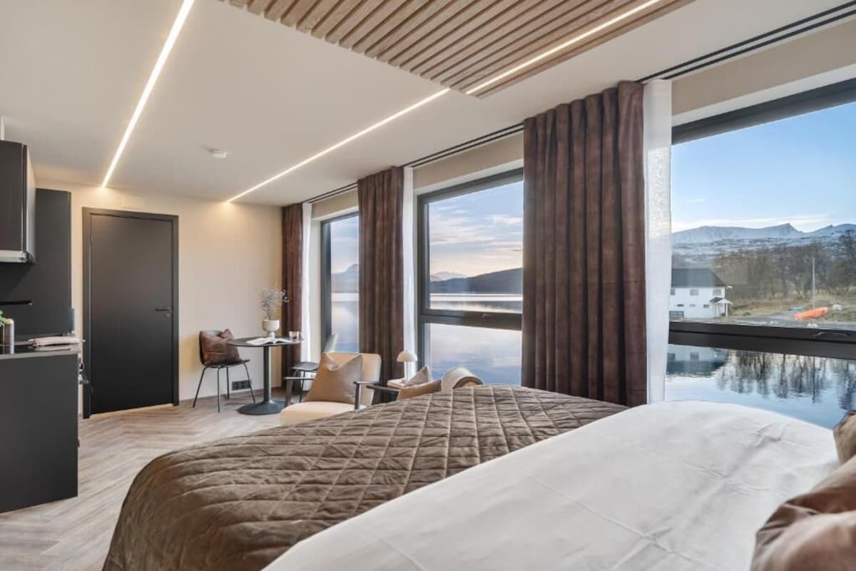 Ein Hotelzimmer mit Bett, Schreibtisch, Stuhl und Blick auf einen See und Berge.