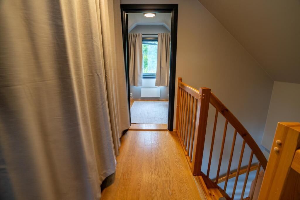 A narrow wooden hallway with a wooden railing, leading to a room with a window and curtains.