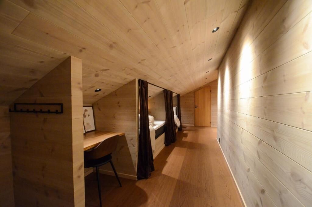 Una habitación con techo inclinado, paredes de madera, un escritorio y una cama con cortinas.
