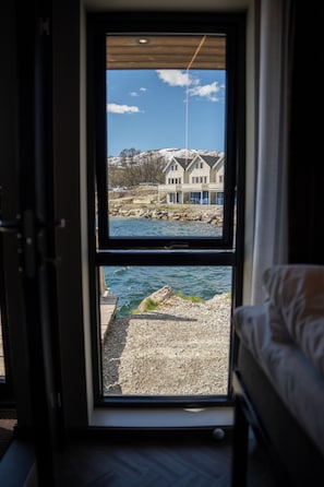 Une chambre avec un lit et une fenêtre donnant sur une maison et l’eau.