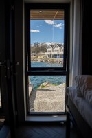 Una habitación con cama, ventana y vista a una casa y al agua.