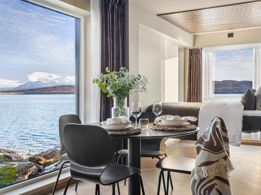 Ein Zimmer mit Esstisch für zwei Personen, einer Couch und Blick auf einen See und Berge.