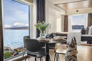 A room with a dining table set for two, a sofa, and a view of a lake and mountains.