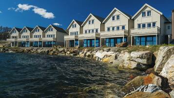 A row of coastal houses with balconies, situated by a rocky shoreline with clear blue water.