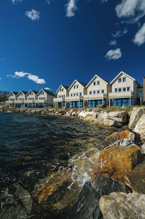 A row of coastal houses with balconies, situated by a rocky shoreline with clear blue water. - Steam Pier Adventure Hotel (Tromsø)