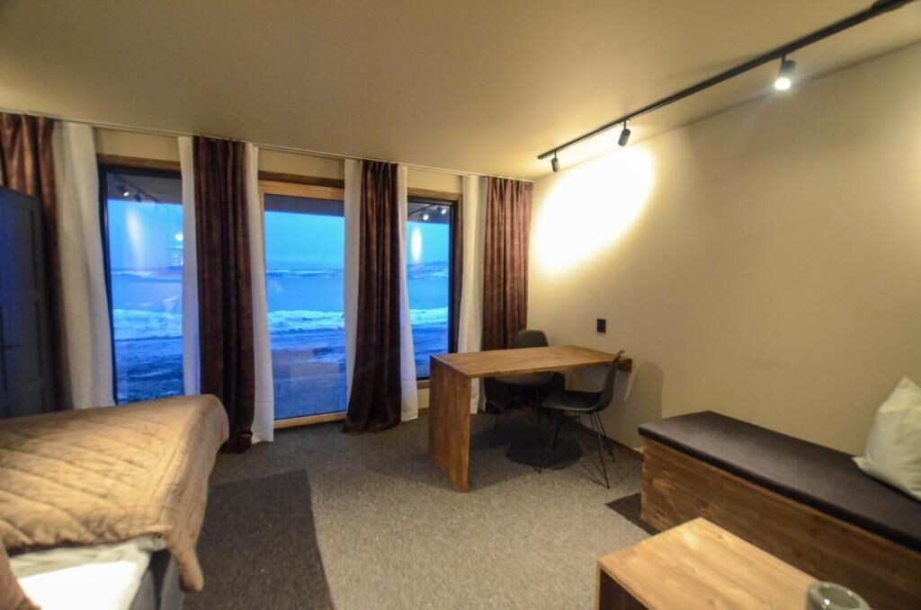 A hotel room with a bed, a desk, a chair, a sofa, and a large window with curtains.