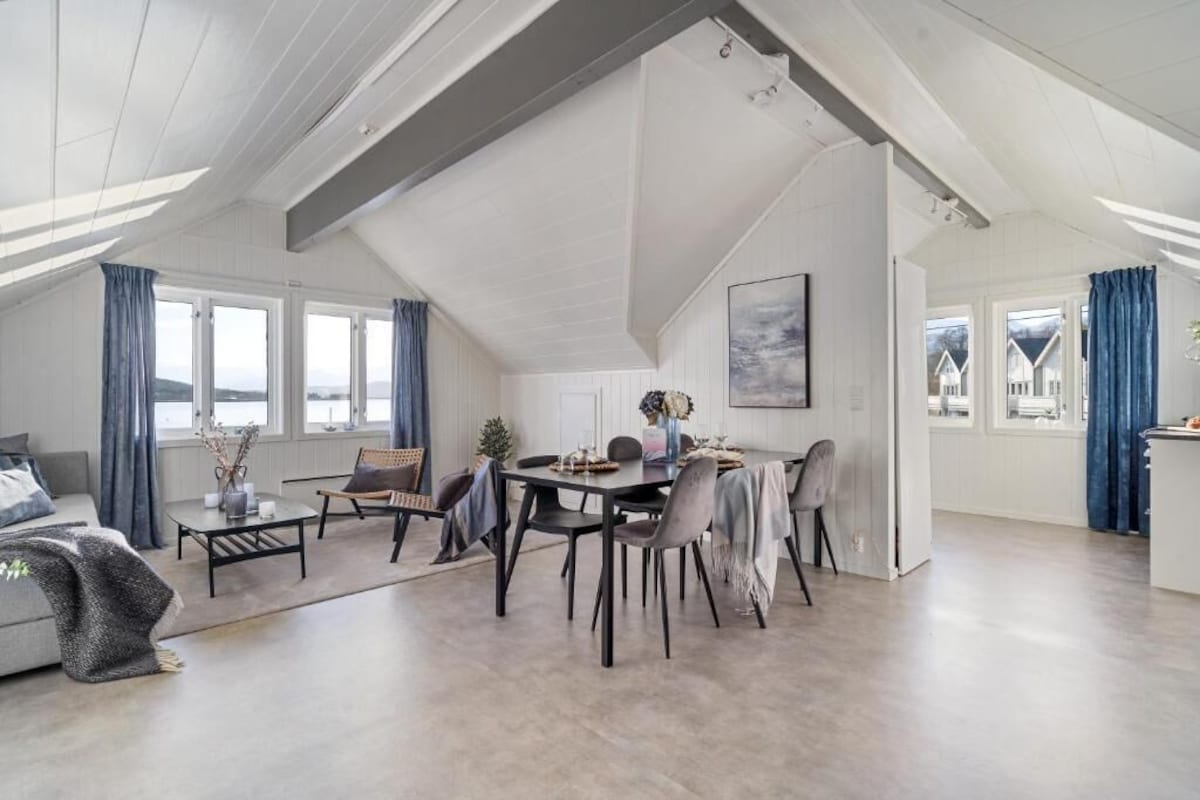 Ein großzügiger Wohnbereich im Loft-Stil mit Esstisch und Stühlen, einer Couch und Blick auf Häuser durch große Fenster.