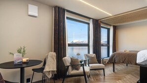 A modern hotel room with a large window, a bed, a small table with a candle, and two chairs. - Steam Pier Adventure Hotel (Tromsø)