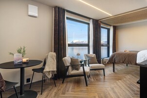 Habitación de hotel moderna con un ventanal grande, una cama, una mesita con una vela y dos sillas.
