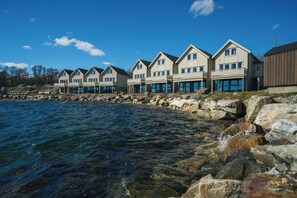 A row of coastal houses with large windows, a rocky shoreline, and clear blue sky. - Steam Pier Adventure Hotel (Tromsø)