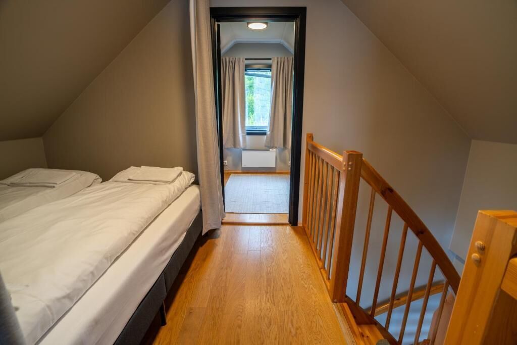 A narrow hallway leading to a bedroom with a wooden floor and a wooden railing.