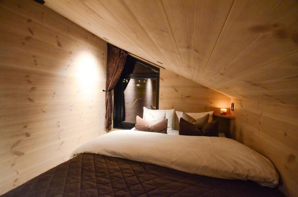 A cozy room with a bed, a nightstand, and a window with curtains.