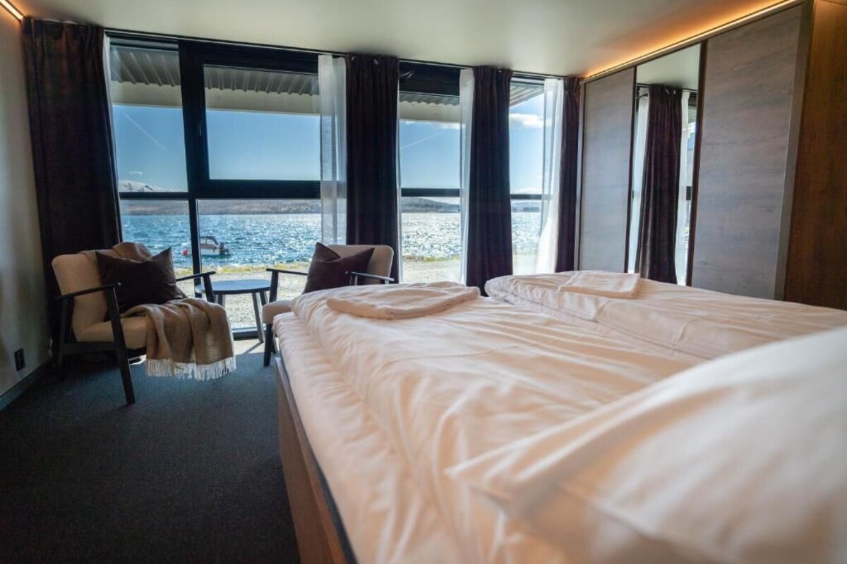 Ein Hotelzimmer mit einem großen Bett, einem Sessel, einem kleinen Tisch und Meerblick durch große Fenster.
