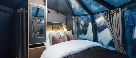 Un dormitorio con tragaluz, una cama, una mesita de noche y un espejo.