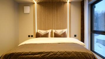 A hotel room with a bed, a window, and a wall-mounted light fixture.