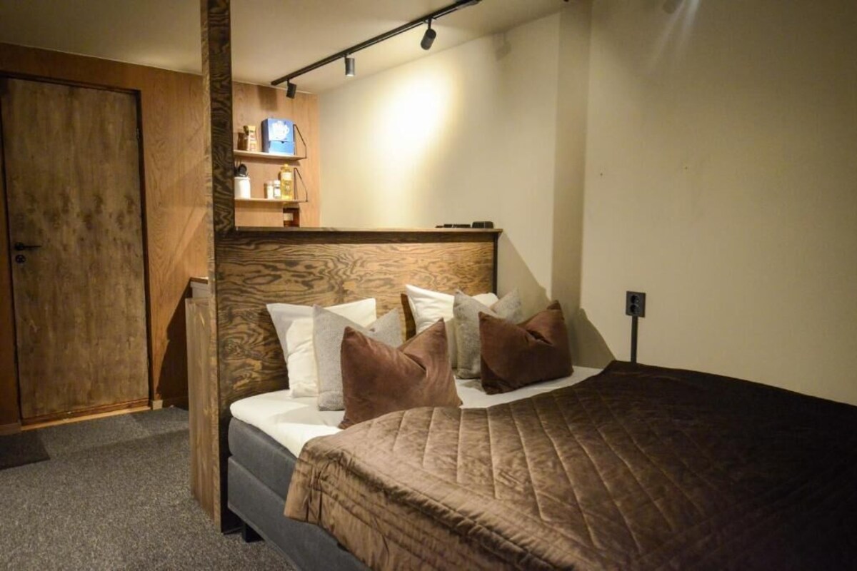 Ein Schlafzimmer mit einem hölzernen Kopfteil, einem Bett mit vielen Kissen, einem Nachttisch und einem Regal mit Gegenständen.