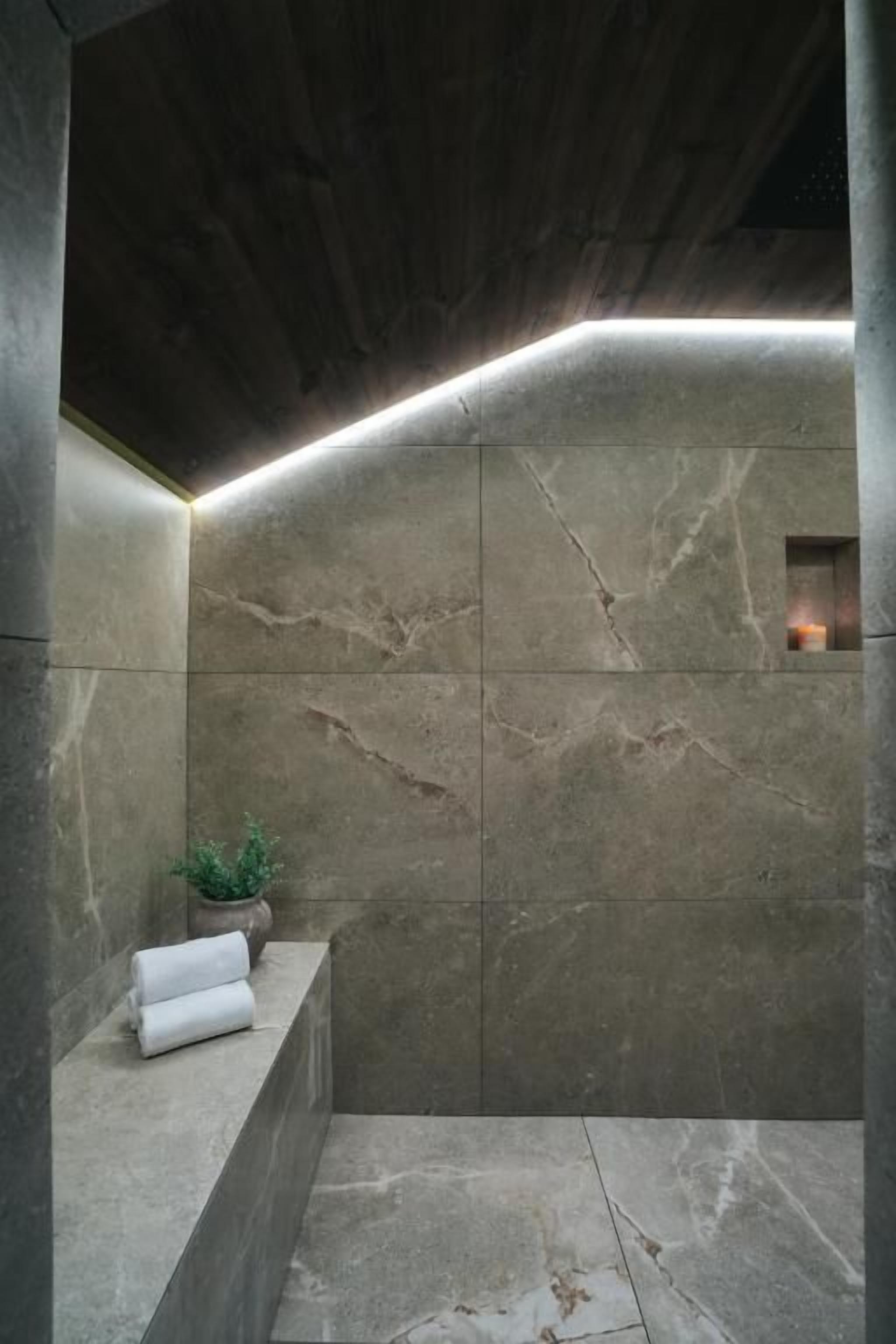 A modern bathroom with a stone wall, a small plant, and a towel on a ledge.