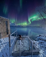 Una persona en un jacuzzi al aire libre con vistas a las auroras boreales.