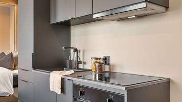 A compact kitchenette with a modern design, including a stainless steel sink, a built-in oven, and a compact stove.