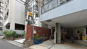 Entrada de un estacionamiento con un letrero de servicio las 24 horas, una pared de ladrillo y una zona cubierta con una bicicleta.