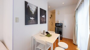 Una habitación pequeña y moderna con una mesa blanca preparada para dos personas, un microondas y una puerta que da a un baño.