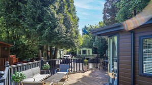 Eine Holzterrasse mit Gartenmöbeln, einer Glastür und Blick auf eine bewaldete Gegend.