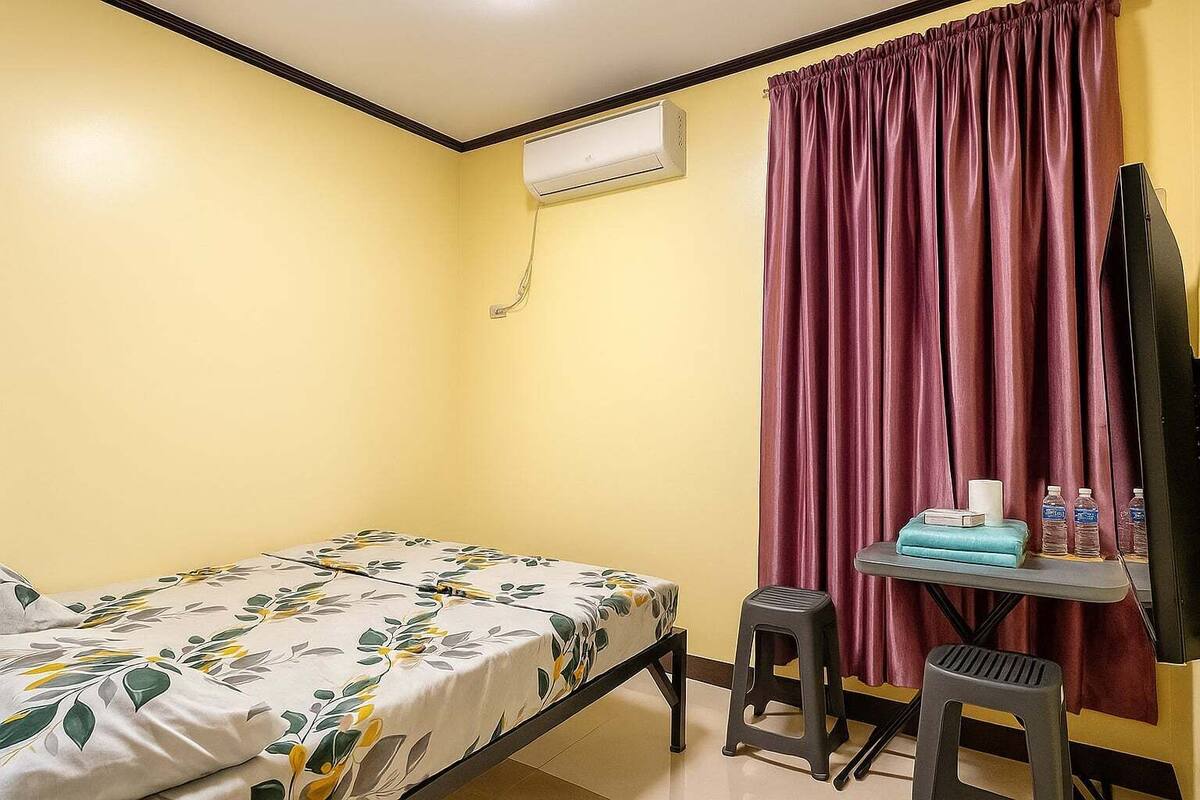 Una habitación pequeña con una cama, un escritorio, una silla, aire acondicionado y una cortina.