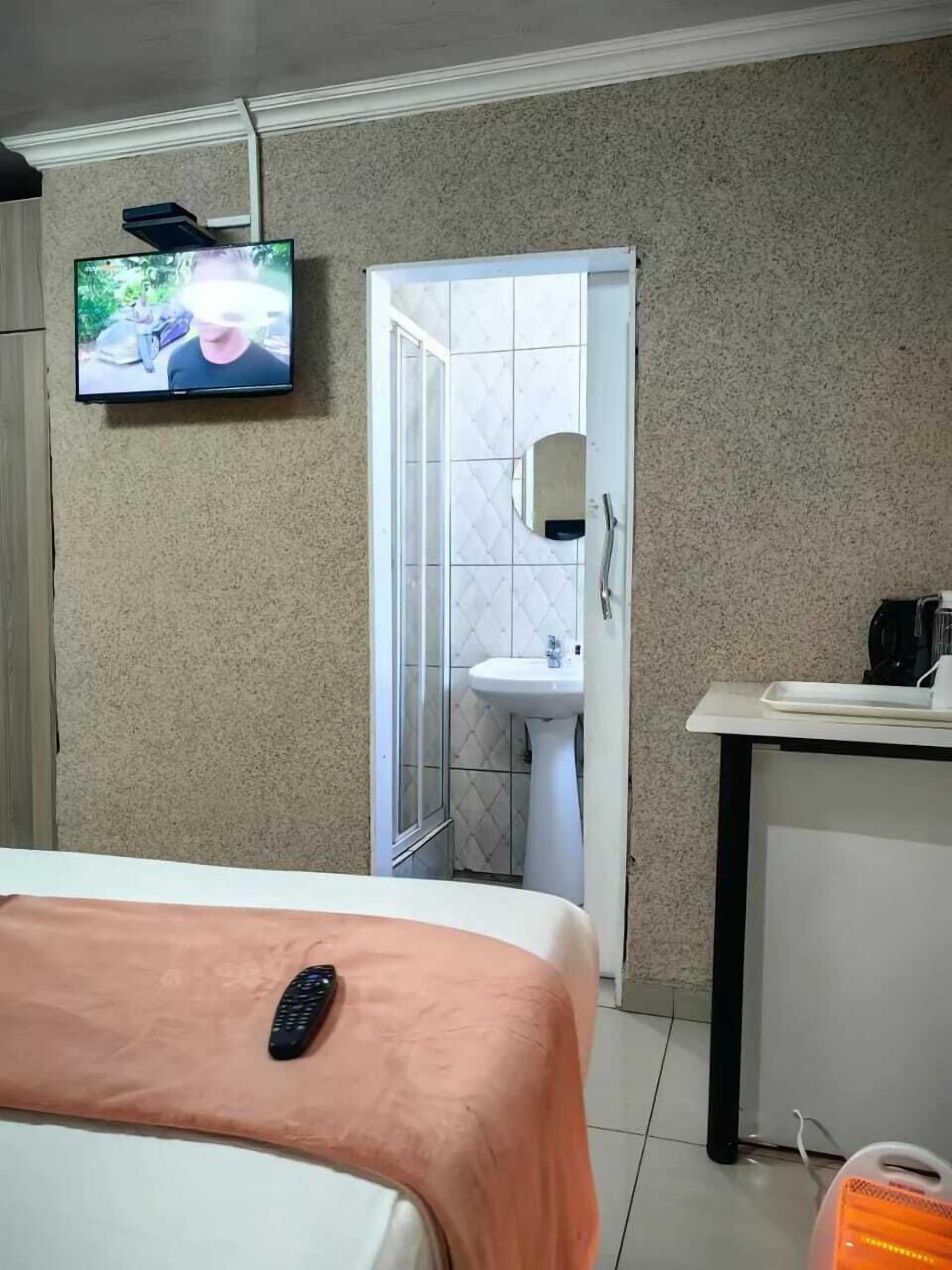 Ett hotellrum med en säng, en tv som är monterad på väggen, ett badrum med handfat och en dusch.