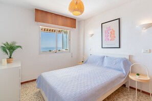 Une chambre à coucher avec un lit, une fenêtre donnant sur un beau paysage, une lampe fixée au mur et un tableau encadré.